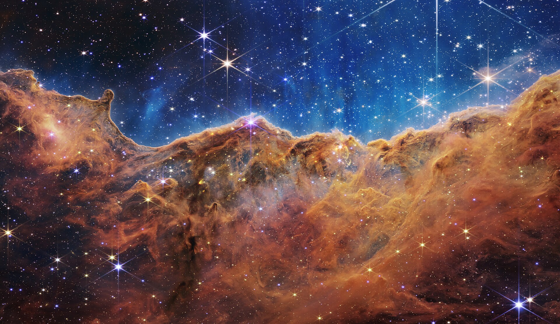 The Cosmic Cliffs in the Carina Nebula, a glowing wall of amber gas beneath a blue field of stars.