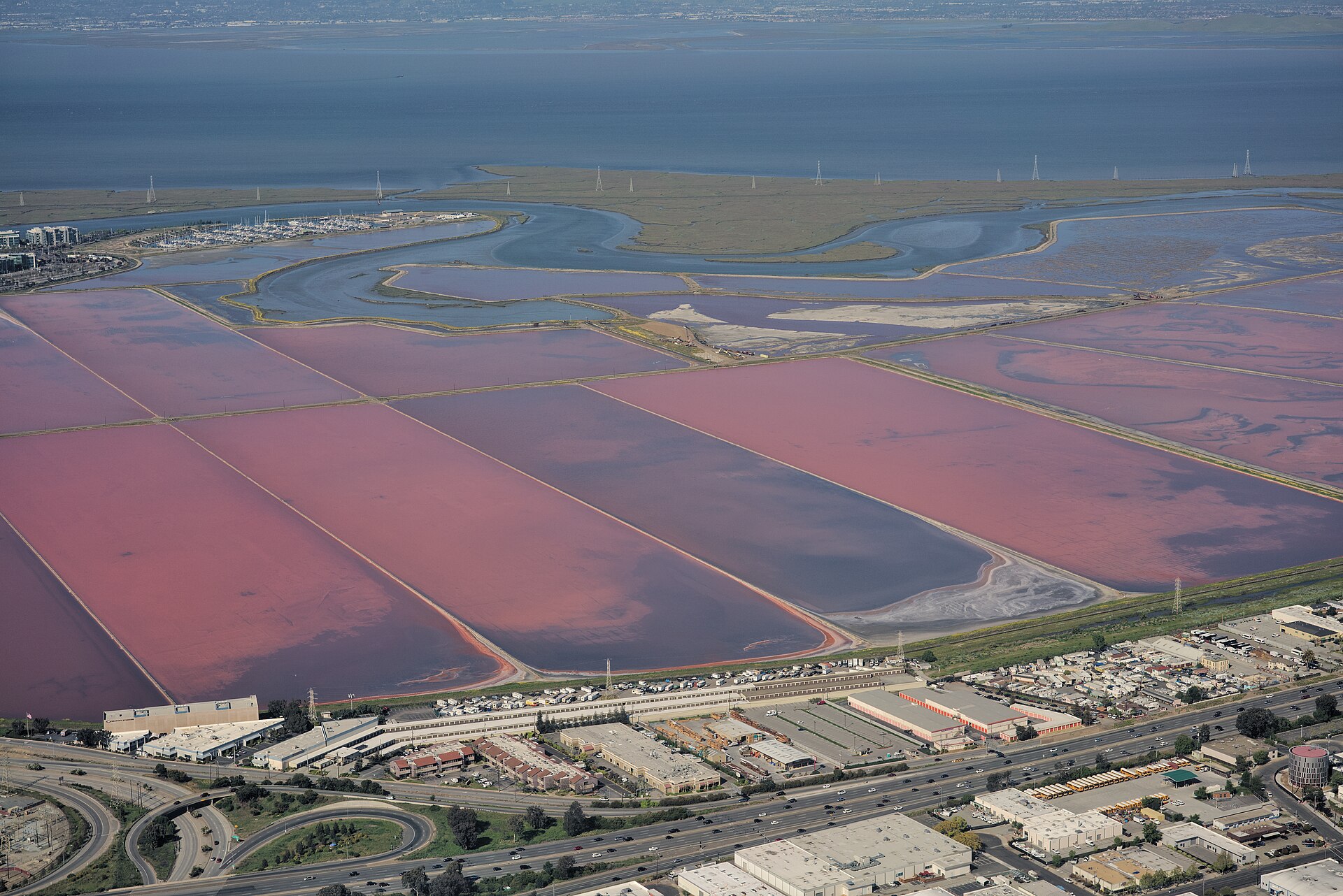 Aerial view of geometric salt ponds around San Francisco Bay in rust, green, tan, and blue.