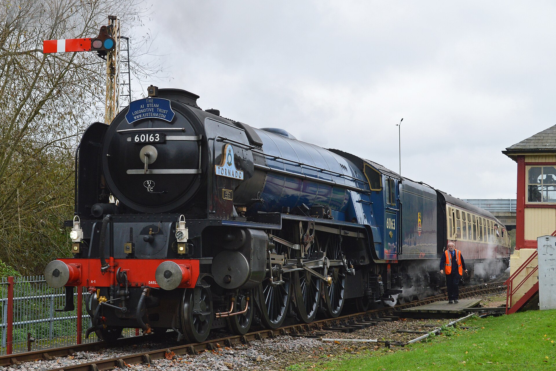 Peppercorn A1 steam locomotive 60163 Tornado in dark blue, steam drifting from its chimney, standing at a heritage railway platform.